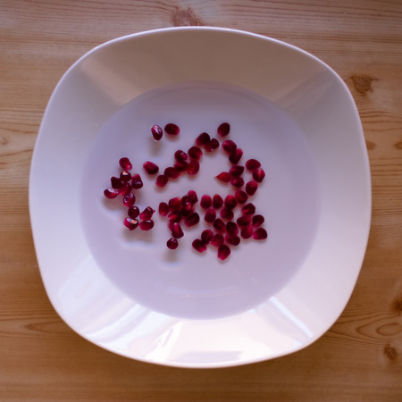 Pomegranate seeds in the water in white bowl on the wooden tableの写真素材