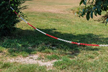 Red and white plastic chain prohibiting passage/parking, hanging on two bushes - Image