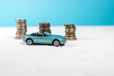 toy blue car cabriolet on a white road. behind lie money coinsの写真素材