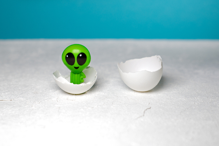 green extraterrestrial is smiling in the eggshell. blue background