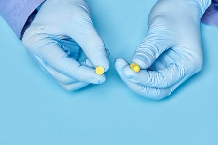 doctor holds yellow pills in his hands. medical worker in gloves. pharmacology. blue backgroundの写真素材