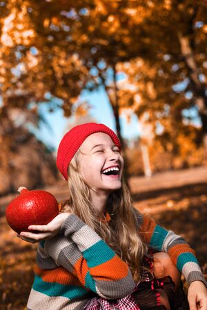 Autumn portrait of happy girl in red hat and sweater. teenager holds an orange pumpkin and smilesの写真素材