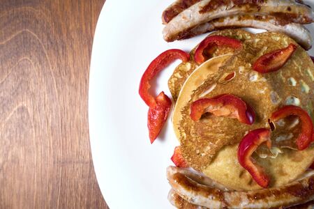 fried sausages pancakes and red pepper lie on a white plate. wooden background. copy spaceの写真素材