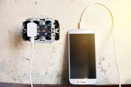charging the phone. cable in a broken outlet. concrete background