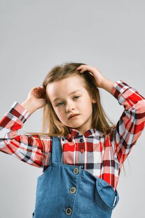 Portrait of a fashionable little girl in a plaid shirt and denim overalls. studio fashion shootingの写真素材