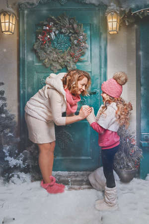 happy family in christmas and new year near the house in the evening. mom hugs her daughter by the palms and holds hand by hand in the street.の写真素材