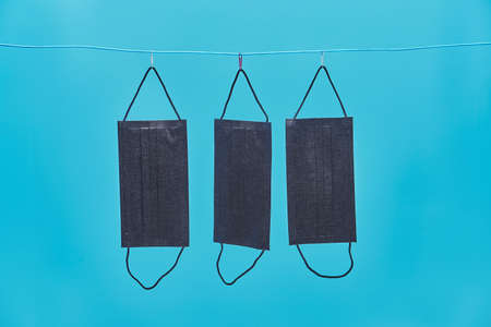 black medical masks are dried on a clothesline. reusable protective face masks. blue background