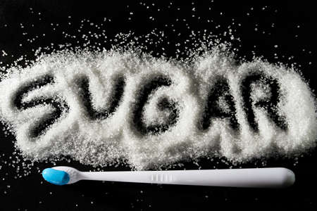new white toothbrush and the inscription of sprinkled sugar on a dark background. dental treatment and caries conceptの写真素材