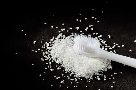 new white toothbrush and a handful of sprinkled sugar on a dark background. dental treatment and caries conceptの写真素材