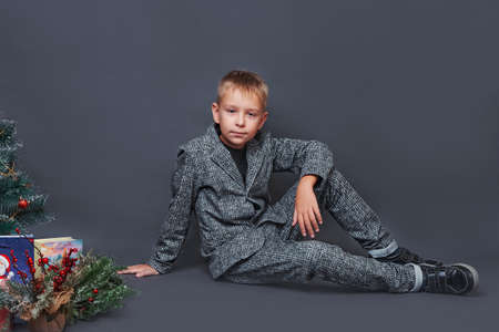 portrait of little boy in suit pants jacket shirt near the christmas tree. stage. gray background. studioの写真素材