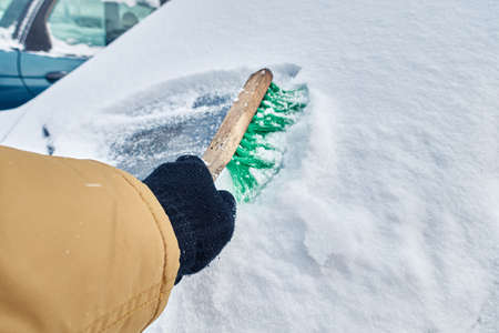 man brushes a car from snow in winterの写真素材
