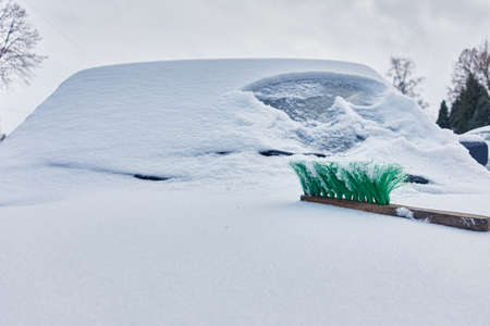 green snow brush lies on the hood of a snow-covered carの写真素材