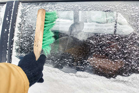 man brushes a car from snow in winter