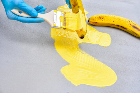 man in blue gloves painting banana with brush with yellow paintの写真素材