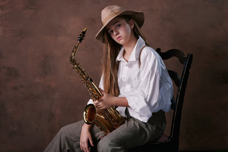 glamorous portrait of a girl with a saxophone. saxophonist with a musical wind instrument sits on a...