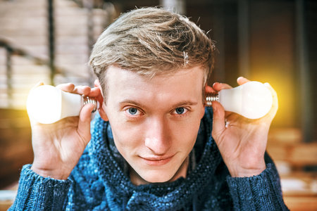 young man holds glowing ice light bulbs in his hands near his head