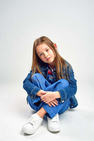 pensive little girl in jeans sits on the floor. studio shootingの写真素材
