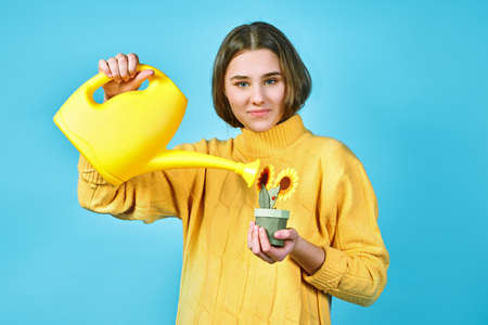 girl in yellow sweater pours flowers from watering can. blue backgroundの写真素材