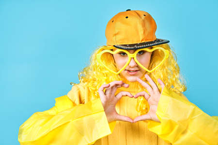 happy teenager holding heart shaped glasses in his hands. young girl with yellow hair in a cap. blue...