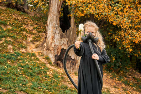 little girl with white rose in the hands of hay. child in gas mask with breathing apparatus backpack behind his back. epidemic ecology conceptの写真素材