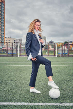 portrait of beautiful girl football player in man's suit on soccer field with ballの写真素材