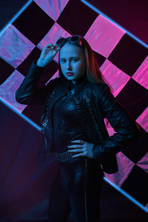 portrait of girl in neon light in racing goggles in leather jacket against the background of the finish flagの写真素材