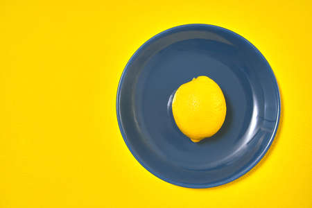 one yellow lemon on blue plate. copy spaceの写真素材