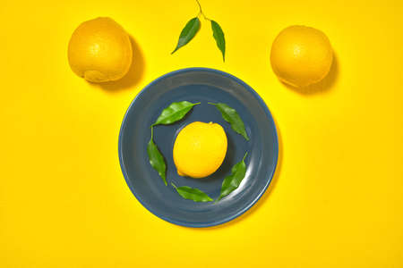 whole yellow lemons with leaves on the table on a blue plateの写真素材