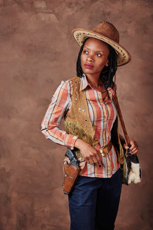 portrait of an african american girl cowboy with hat and pistol in holster. photo in the studio....