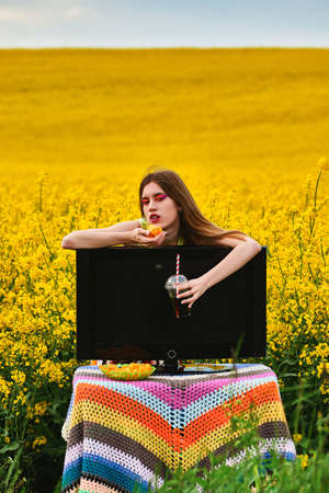 young girl eating chips and drinks a drink in field with tv. vacation concept. creative