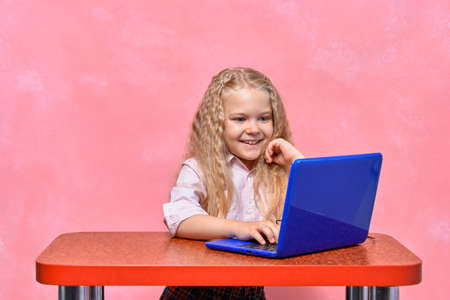 online training. little schoolgirl learns remotely on laptop. pink background