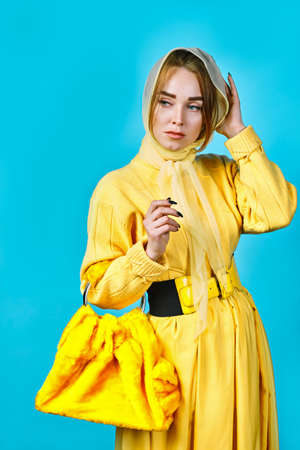 portrait of young woman in yellow sweater with fur bag in her hands. blue backgroundの写真素材