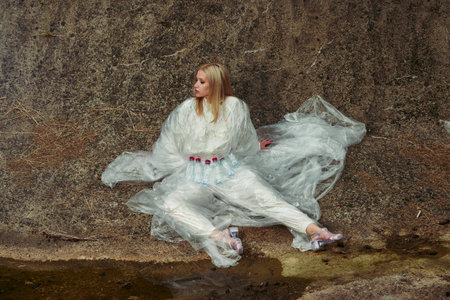 Fashion concept. Girl model in cellophane sits on the ground. Creative vogue