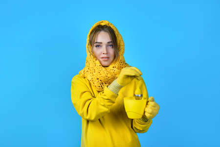 girl makes tea in a mug. woman in yellow clothes and a scarf. blue backgroundの写真素材