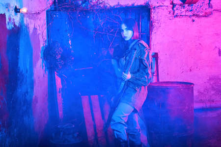 portrait in neon light of a beautiful girl in an abandoned building with a metal pipe in her hands