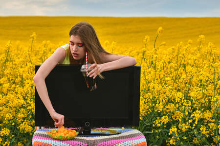 young girl eating chips and drinks a drink in field with tv. vacation concept. creative