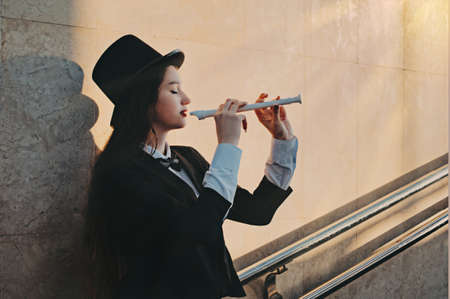 girl musician plays the flute. woman in a suit and bow tie in a top hat in an underpassの写真素材