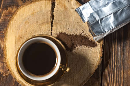 brewed black coffee in a golden cup. coffee pot and bag of spilled ground coffeeの写真素材