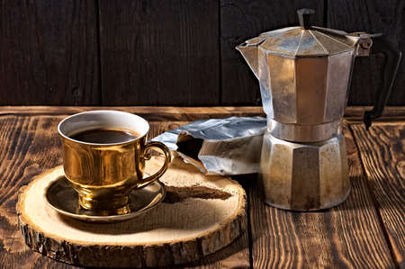 brewed black coffee in a golden cup. coffee pot and bag of spilled ground coffeeの写真素材