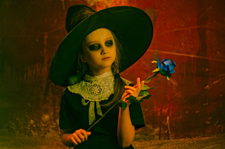 Halloween portrait of a little girl in a hat with a blue rose flower in her hands