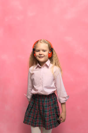 little girl listens to music in wireless headphones. pink backgroundの写真素材