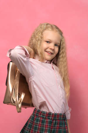 portrait of a little girl with a backpack. school girl in uniform. pink backgroundの写真素材