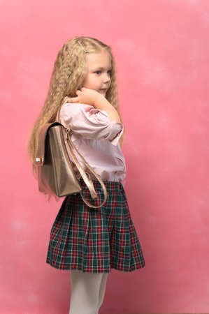 portrait of a little girl with a backpack. school girl in uniform. pink backgroundの写真素材
