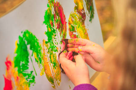 little girl artist with a brush and paints in her hands in autumn in the park draws a landscape with leaves on canvasの写真素材