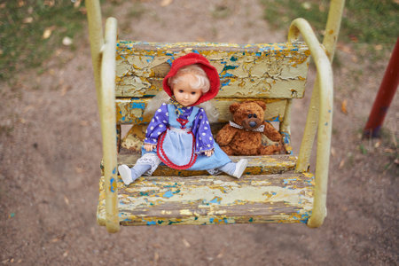 toy doll and teddy bear on a children's swing in the playgroundの写真素材