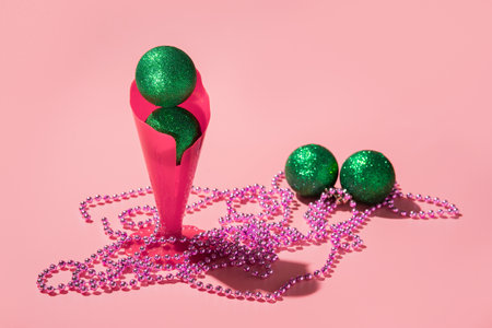Green Christmas balls in red gift glass with jewelry. pink background