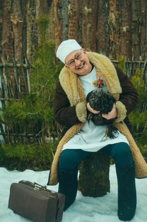 Happy man doctor veterinarian holds a rooster in his hands on the street in winter at the ranchの写真素材