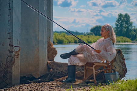 Beautiful woman fisherman is resting on the river. Female is fishing with a rod in gearの写真素材