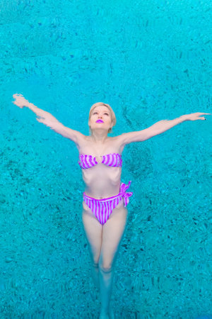 Glamorous woman in a swimming costume in a pool of blue water, hands in the air, praying. view from above.の写真素材