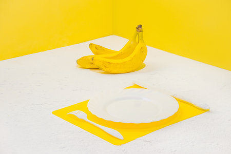 An empty white plate, knife, fork, and banana branch on a restaurant table. minimalist style.の写真素材